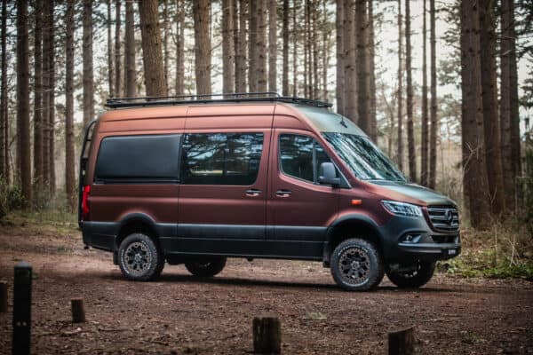 Burgundy chameleon wrapped 4x4 Sprinter with Black Rhino Warlord rims and Dutchvanparts roof rack and Cargo Ladder. The campervan is parked the forest fully blending in.