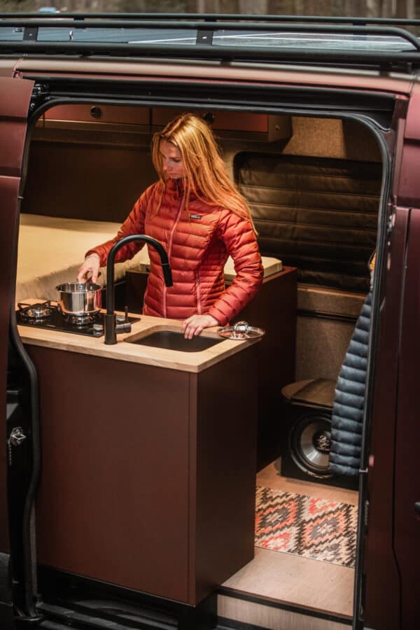Looking into a 4x4 Mercedes Sprinter campervan you see a girl cooking on the SOLO aluminium kitchen galley.